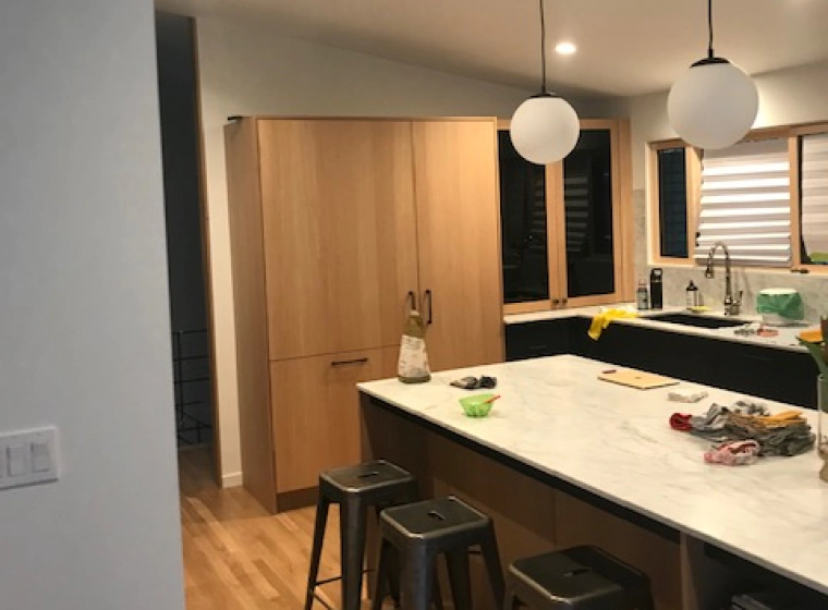 beige kitchen with wooden cabinets and a black countertop with marbled cover and dark grey chairs