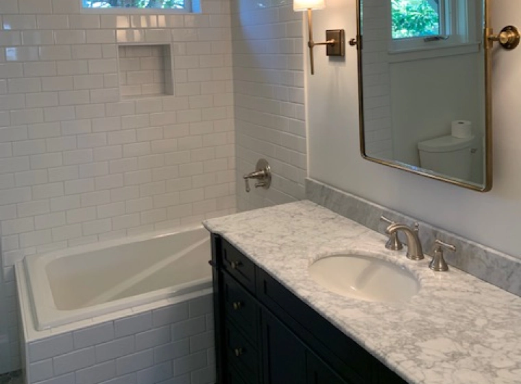 white bathroom with a white bathtub and a black countertop with marbled cover and a square mirror